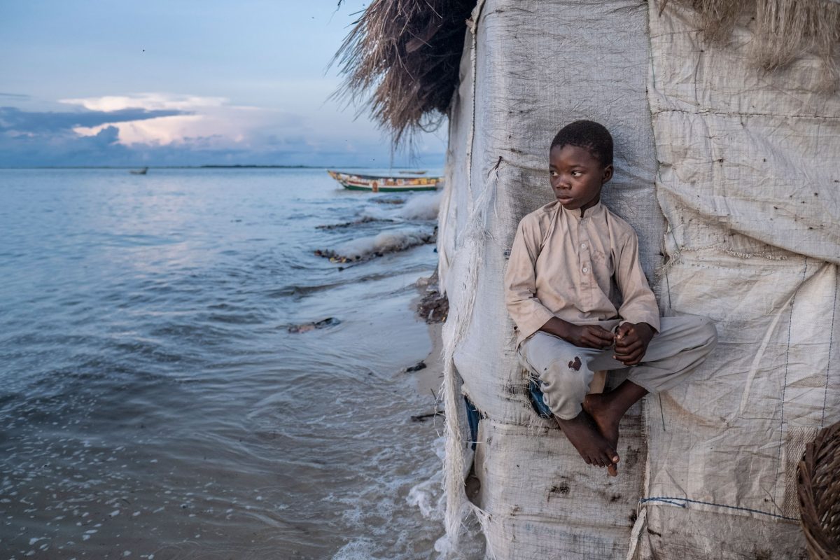 Eight-year-old Ndole Kamara perches on the side of his family’s fish-smoking hut as the rising tide laps against its walls. 
