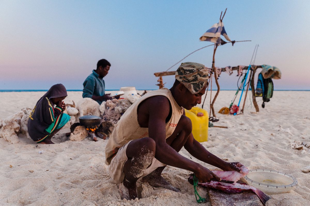 A fisherman fillets fish for supper at his camp on a sandbar.
