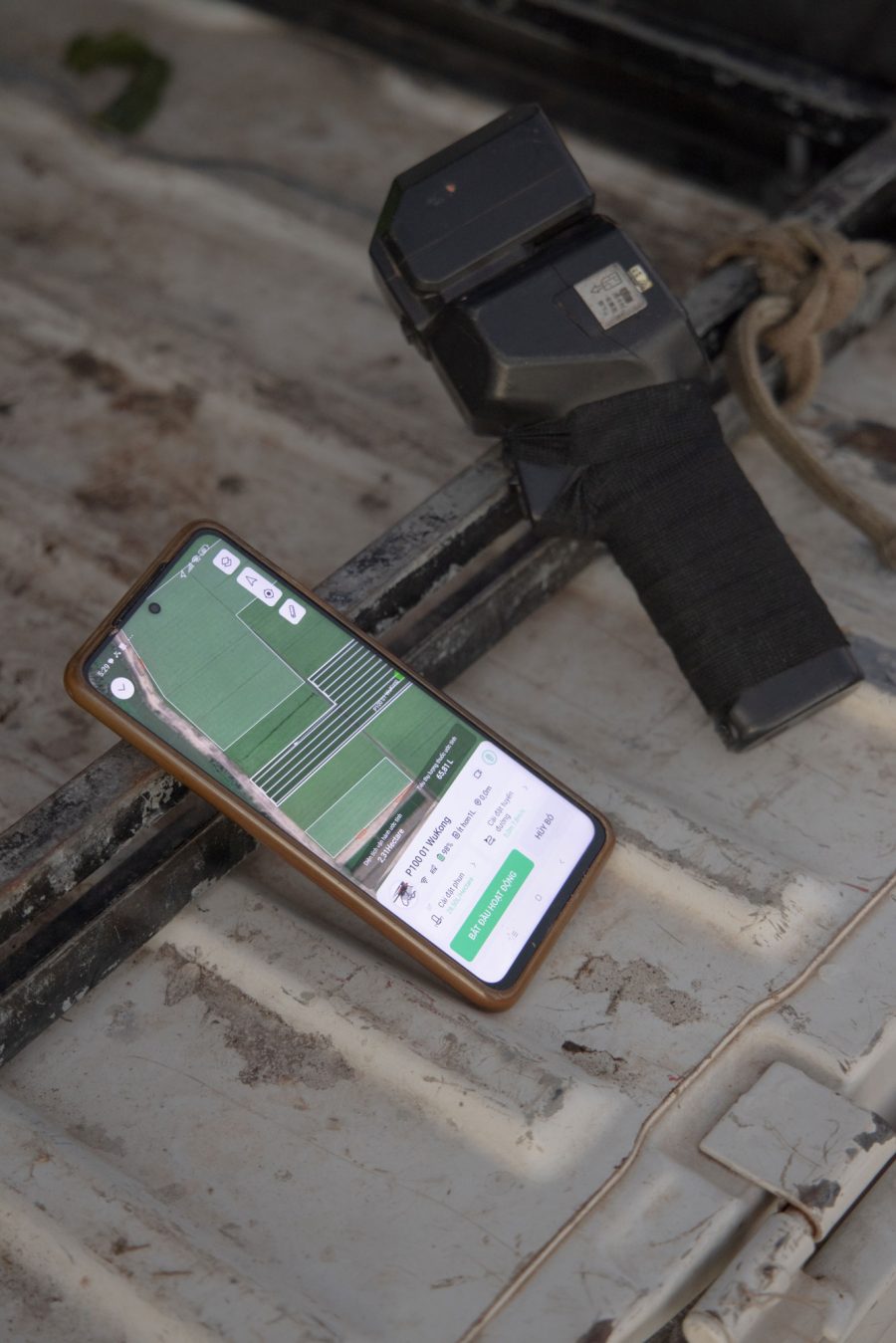 A mobile phone—next to a remote controller—shows a map of a field that will be sprayed by a drone. 