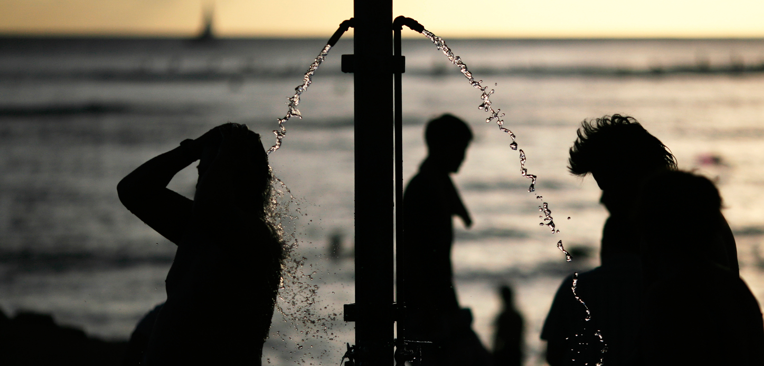 A silhouette of people showering at the waterfront at sunset