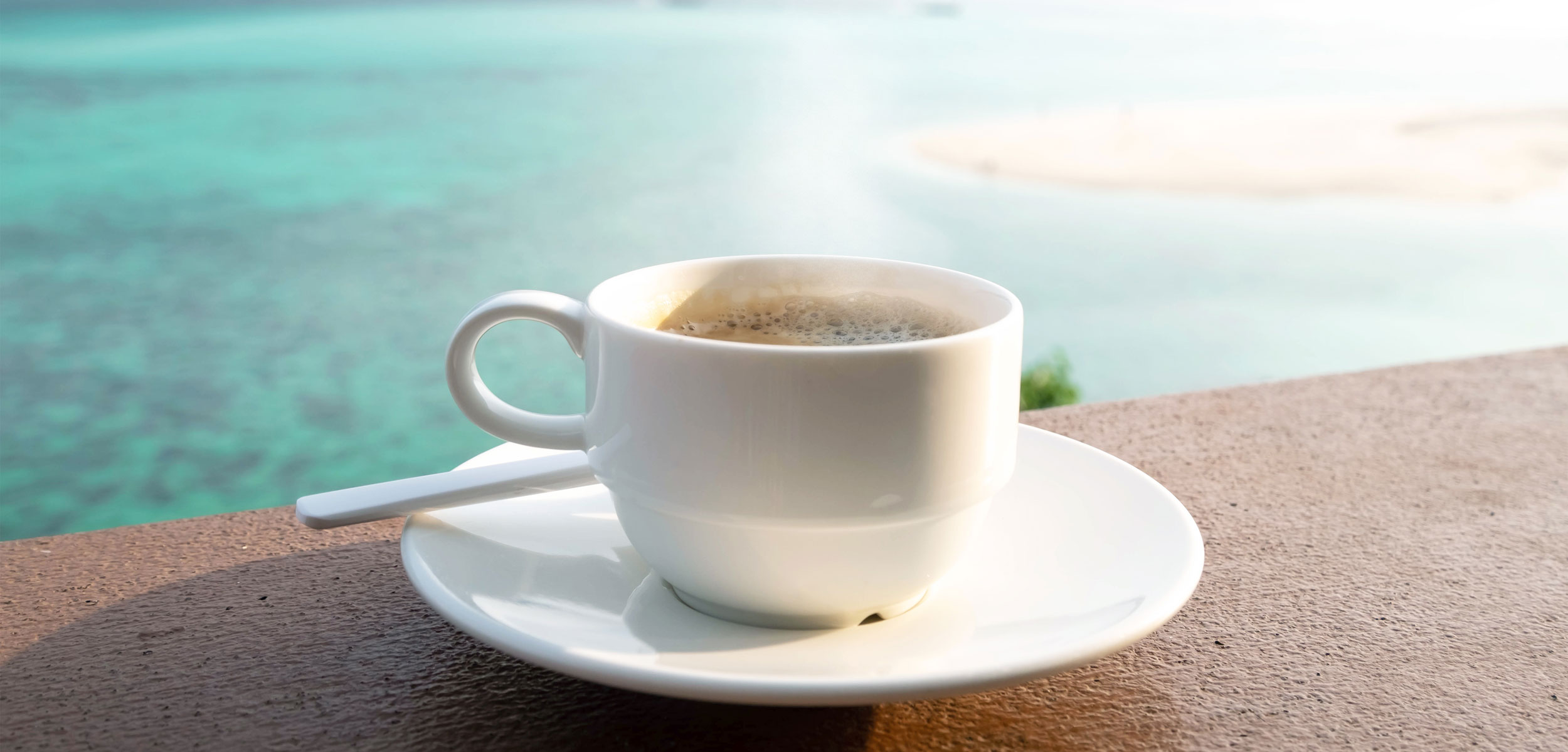 coffee cup on patio ledge next to the ocean