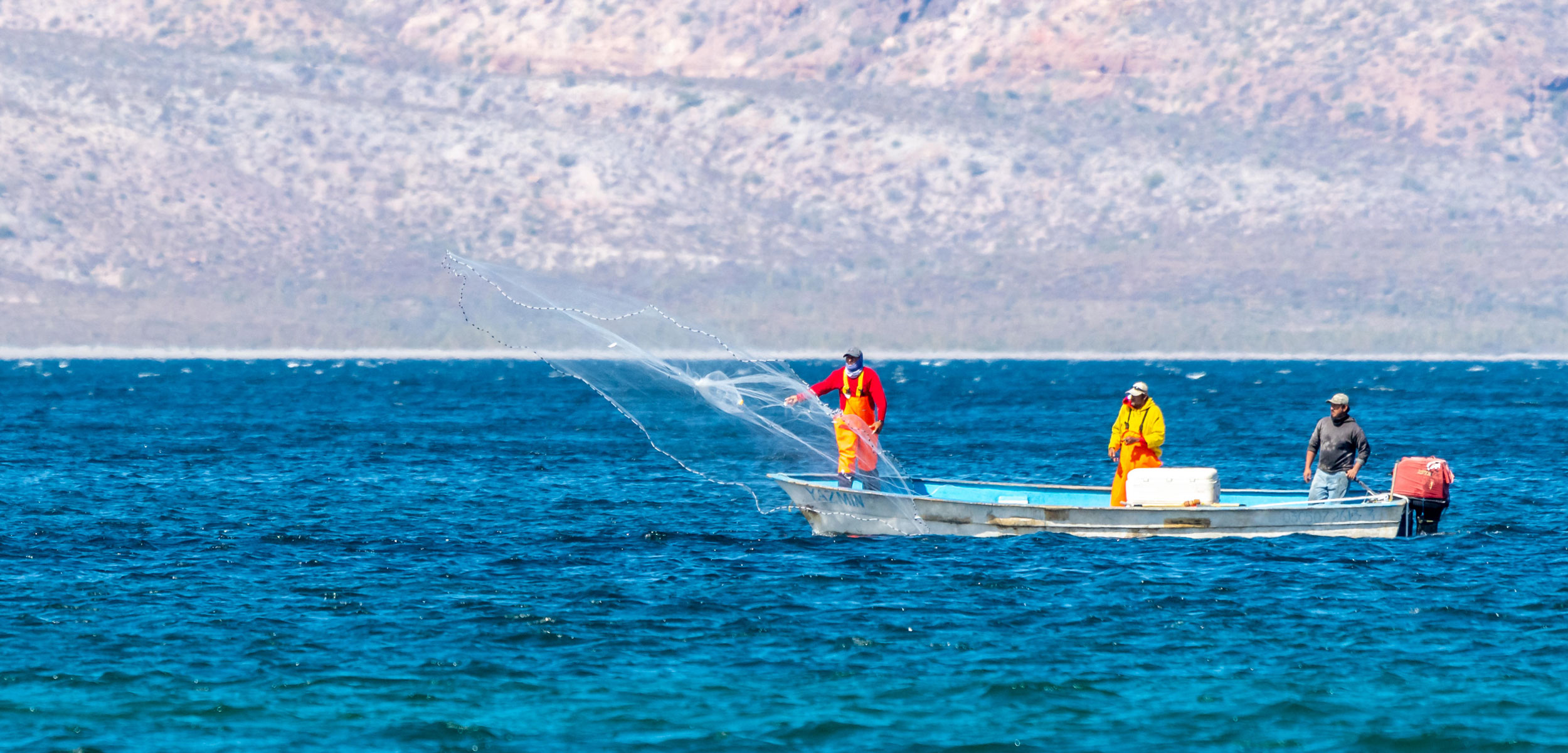 Fishermen in a small boat casting a fishing net in Baja California Sur, Mexico