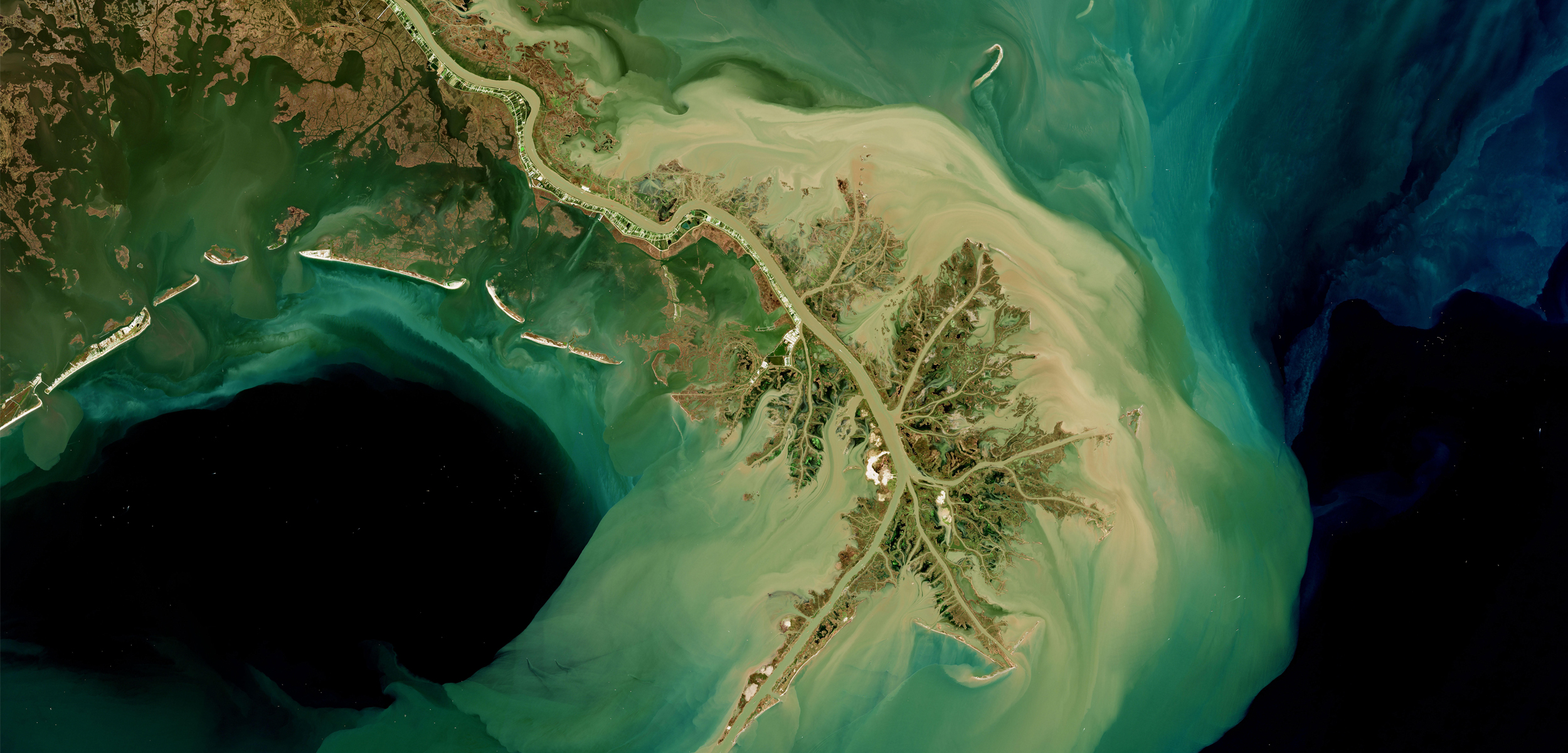 a satellite image of a blue green and black ocean with a sandy colored brown landmass in the middle