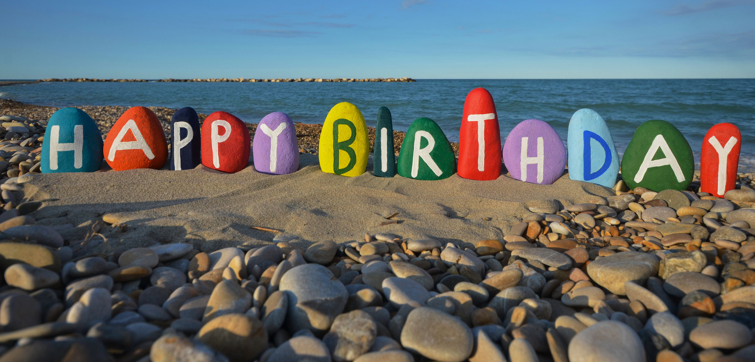 happy birthday painted on stones at the beach