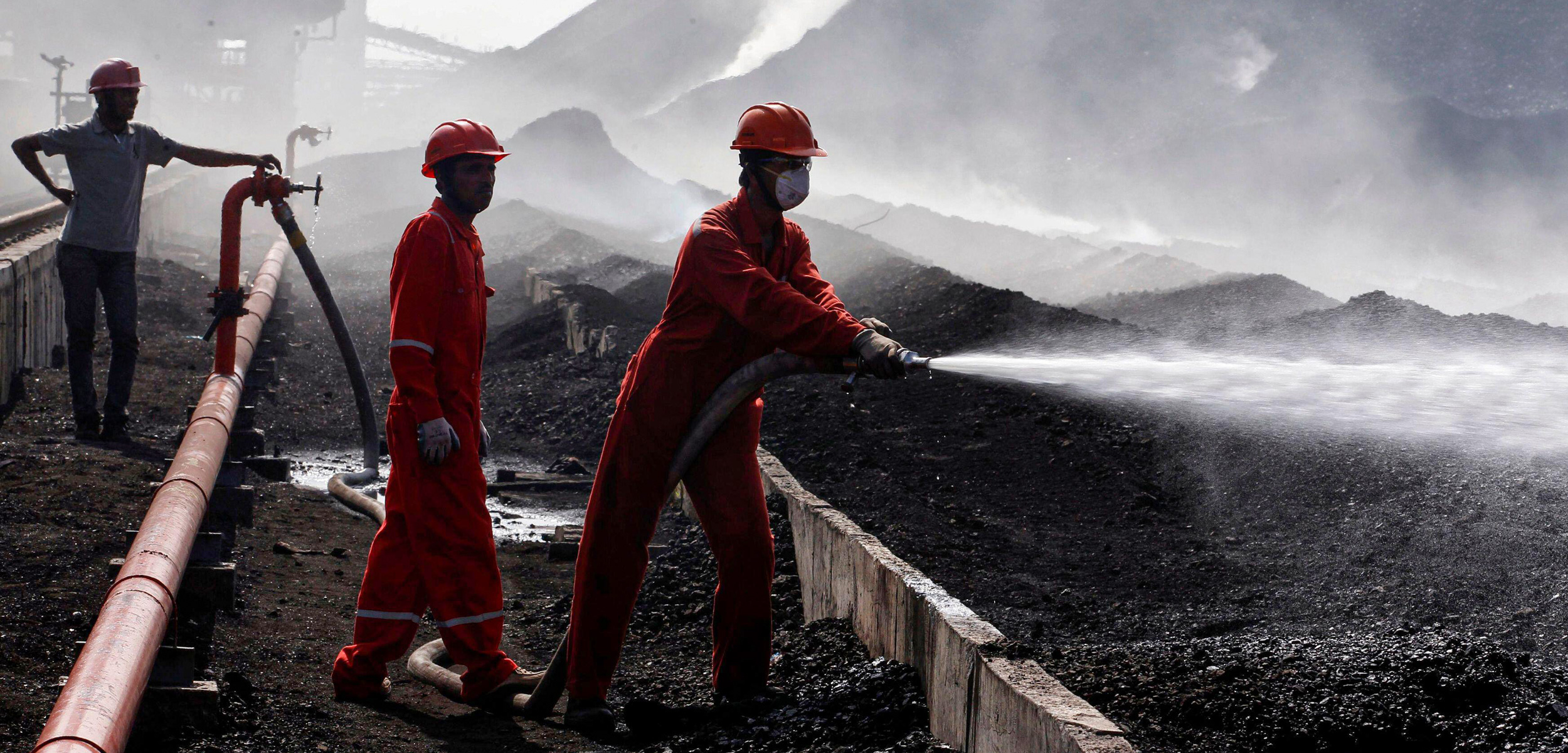 A worker sprays water over piles of coal at Mundra Port Coal Terminal