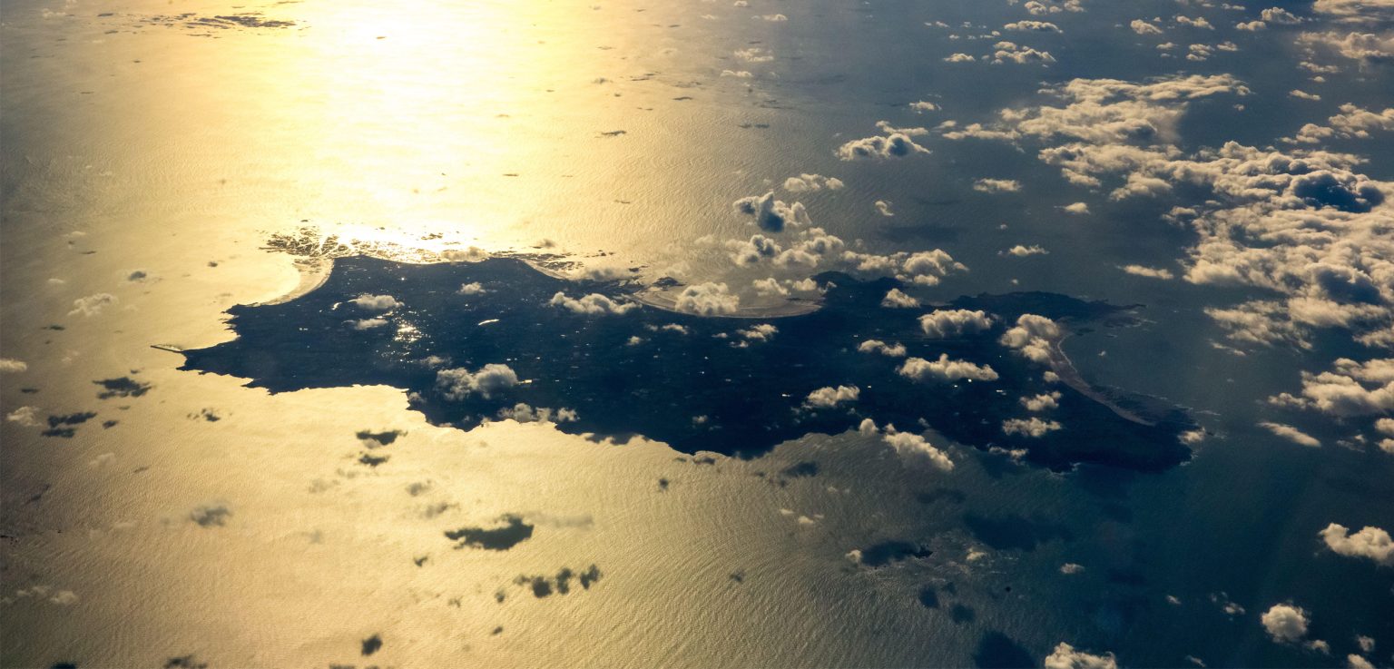 Aerial view of a dark islanf in a rectangular shape with a sunset on the water