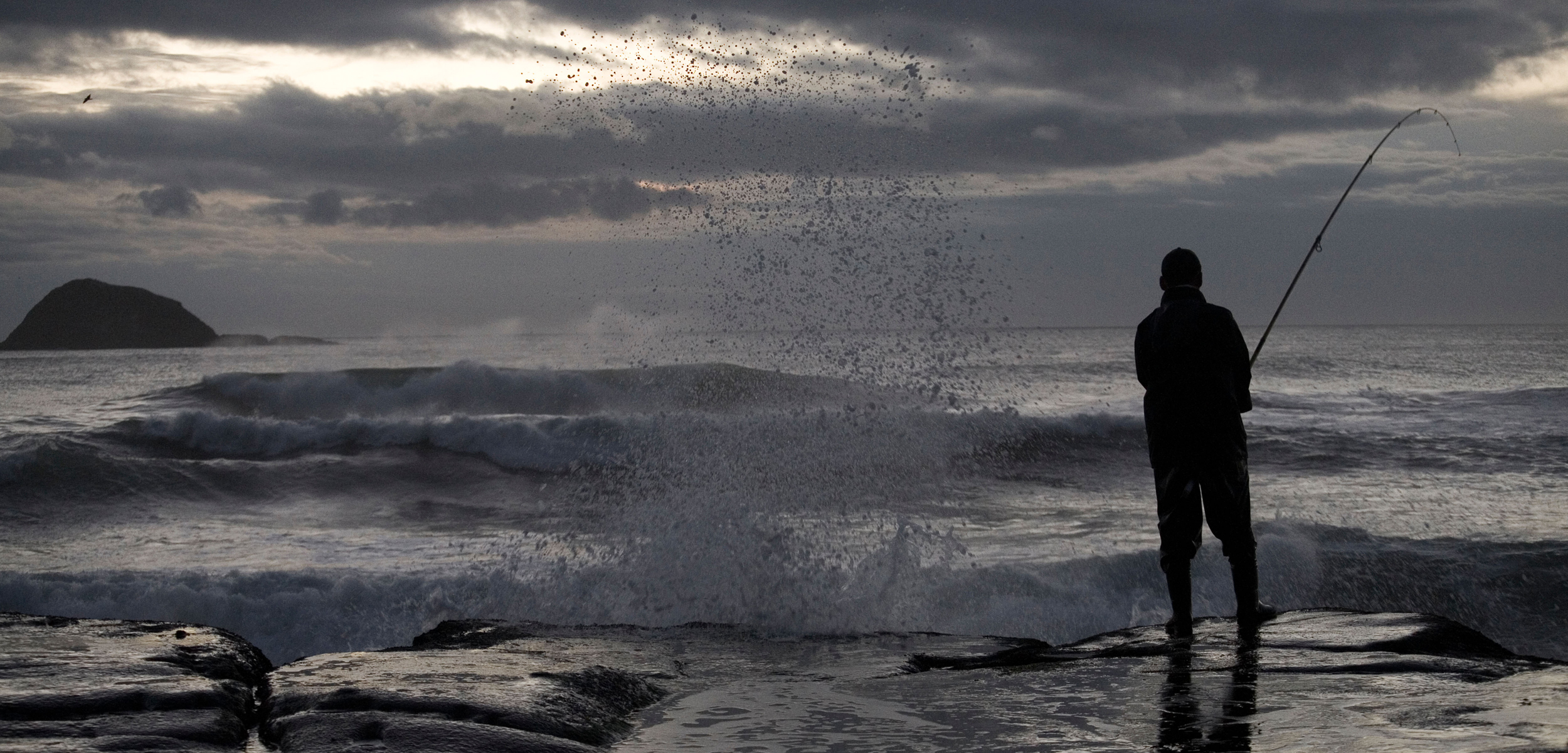 A silhouette of a maori fisherman on the rocks infront of a stormy ocean