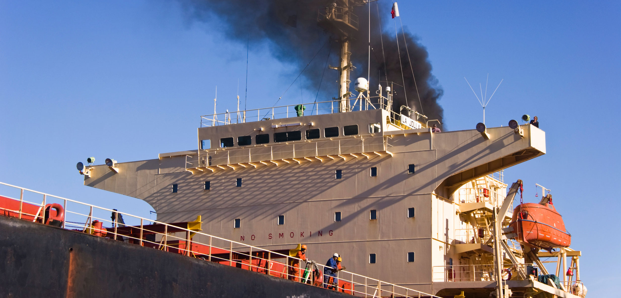 Black smoke rises from ship's funnel as the ship approaches the quay.