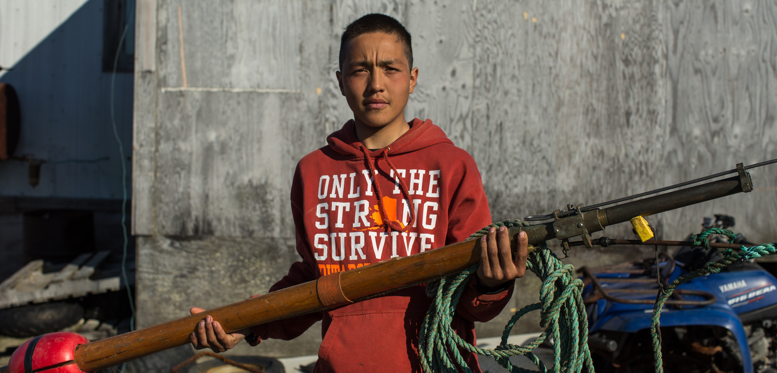Chris Apassingok, 16, holds the darting gun he used to harpoon a whale this spring outside his family’s home in Gambell, Alaska. Photo by Ash Adams