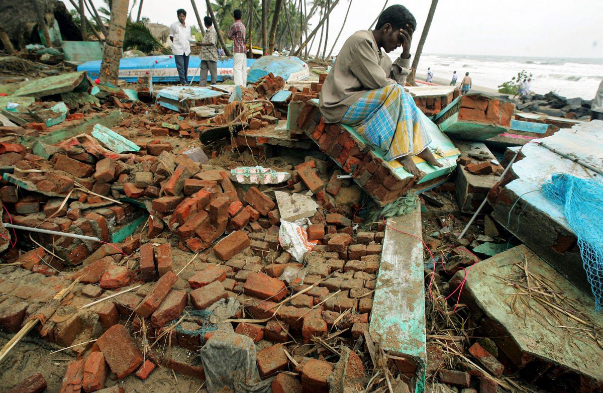 An Indian man holds his head as he sits atop the debris of his house that was destroyed in a tsunami in Cuddalore, India.