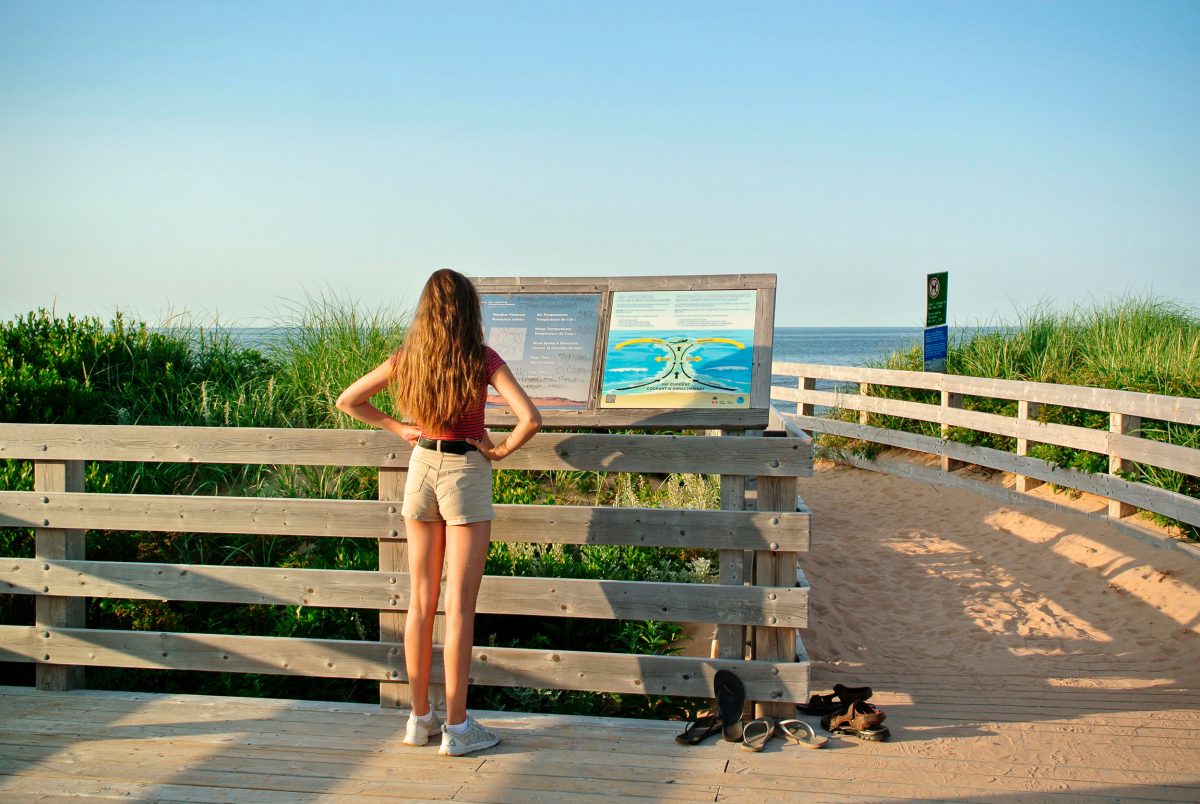 A girl studies an informational sign about rip currents in Greenwich National Park on Prince Edward Island