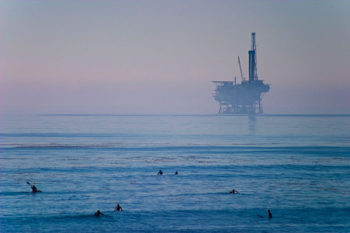 surfers with oil rig in background
